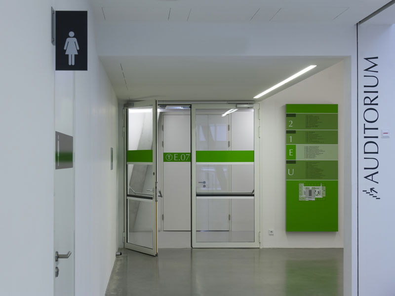 Unterschiedliche Elemente des Leit und Orientierungssystems: Fahnenschild Damen WC, Barrierefreie Kennzeichnung einer Glastüre, Stockwerksübersicht, Beschriftung an der Wand